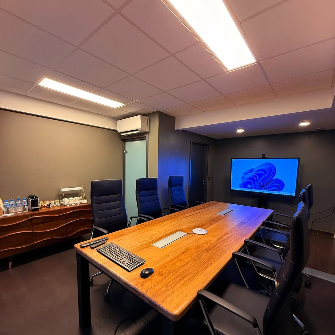 Salle de réunion du cabinet : grande table en bois massif, fauteuils noirs et écran mural